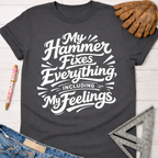 Women's funny woodworking graphic tee shirt for female woodworkers, makers, and DIY builders — Sawdust & Ponytails. Dark gray cotton t-shirt with "My Hammer Fixes Everything, Including My Feelings" in white script.