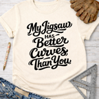 Women's funny woodworking graphic tee shirt for female woodworkers, makers, and DIY builders — Sawdust & Ponytails. Cream t-shirt with "My Jigsaw Has Better Curves Than You" in black script.