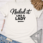 Women's funny woodworking graphic tee shirt for female woodworkers, makers, and DIY builders — Sawdust & Ponytails. Cream t-shirt with "Nailed it LIKE A LADY" in black script and block text.