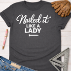 Charcoal gray women's "Nailed it Like a Lady" graphic tee with white text, a nail icon, and rolled sleeves. Women's funny woodworking graphic tee shirt for female woodworkers, makers, and DIY builders — Sawdust & Ponytails.