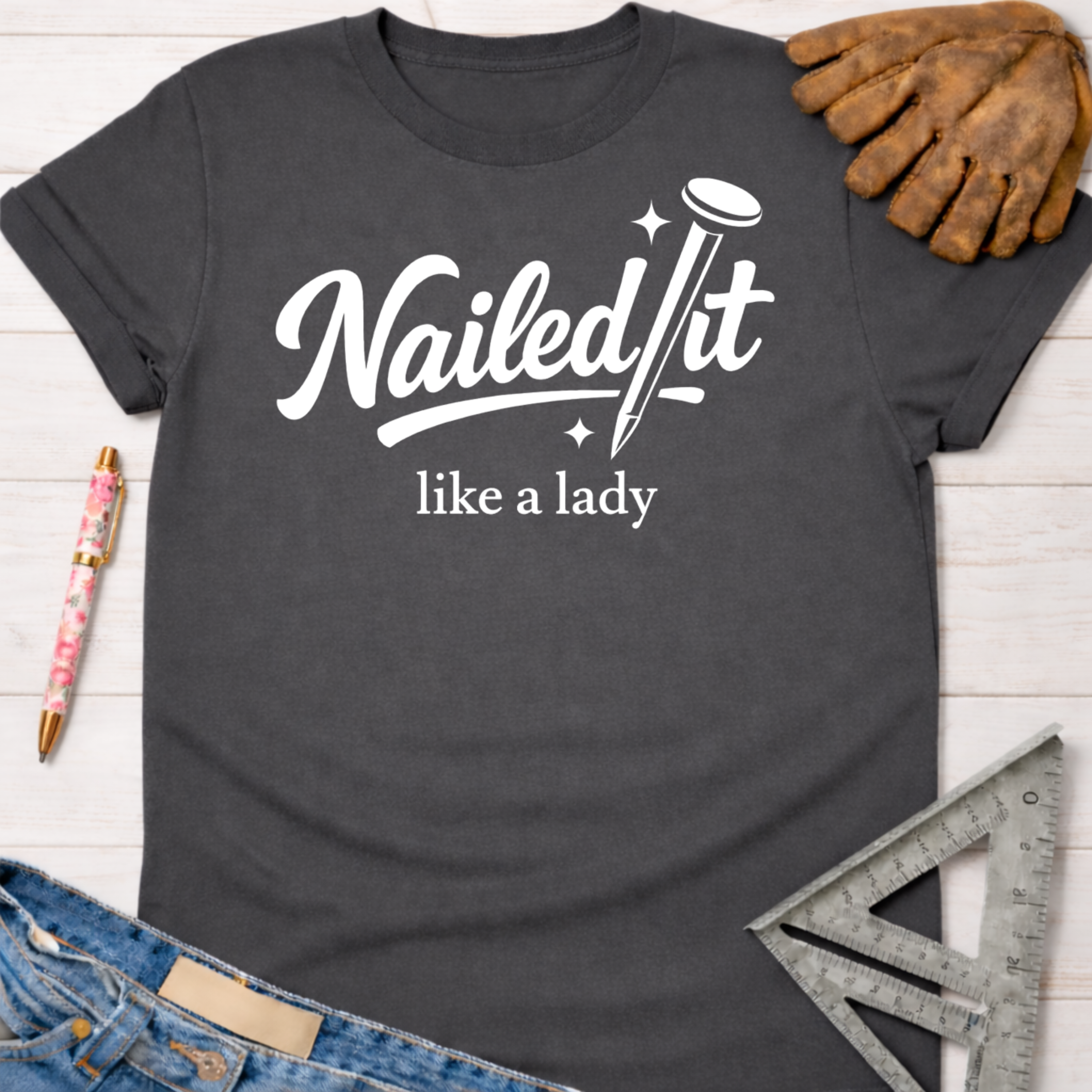 Women's funny woodworking graphic tee shirt for female woodworkers, makers, and DIY builders — Sawdust & Ponytails. Dark gray t-shirt with "Nailed It Like a Lady" text and nail graphic.