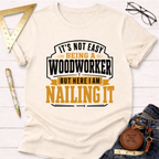 Cream cotton t-shirt with "It's Not Easy Being A Woodworker But Here I Am Nailing It" graphic in black and gold.
