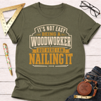 Olive green "Nailing It" t-shirt for woodworkers, featuring a bold graphic design in cream and orange.