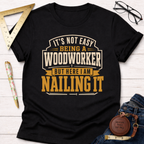 Black cotton "Nailing It" t-shirt with "It's Not Easy Being a Woodworker But Here I Am Nailing It" graphic.