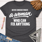 Charcoal gray cotton t-shirt with "Never Underestimate a Woman Who Can Fix Anything" in white text. Women's funny woodworking graphic tee shirt for female woodworkers, makers, and DIY builders — Sawdust & Ponytails.