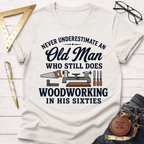 Cream t-shirt with "Never Underestimate An Old Man Who Still Does Woodworking In His Sixties" text and tools.