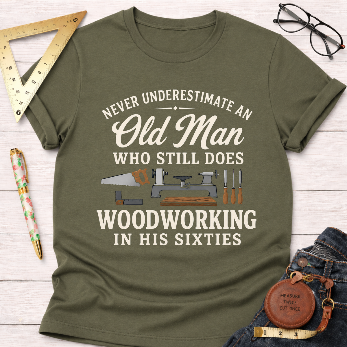 Olive green t-shirt with "Never Underestimate An Old Man Who Still Does Woodworking In His Sixties" text and tools.