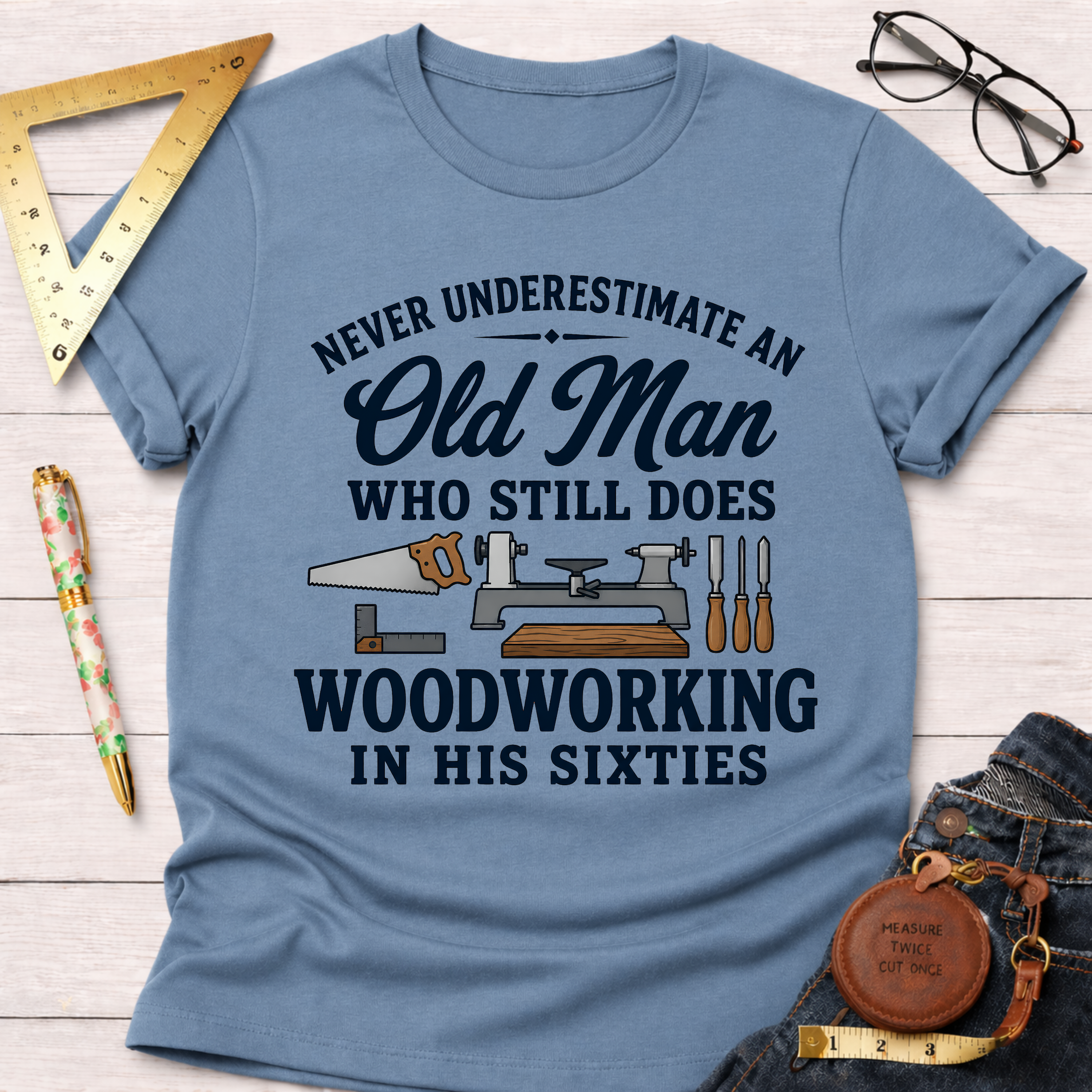 Light blue t-shirt with "Never Underestimate An Old Man Who Still Does Woodworking In His Sixties" text and tools.