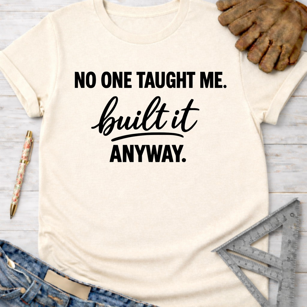 Women's funny woodworking graphic tee shirt for female woodworkers, makers, and DIY builders — Sawdust & Ponytails. Cream t-shirt with "NO ONE TAUGHT ME. built it ANYWAY." text.