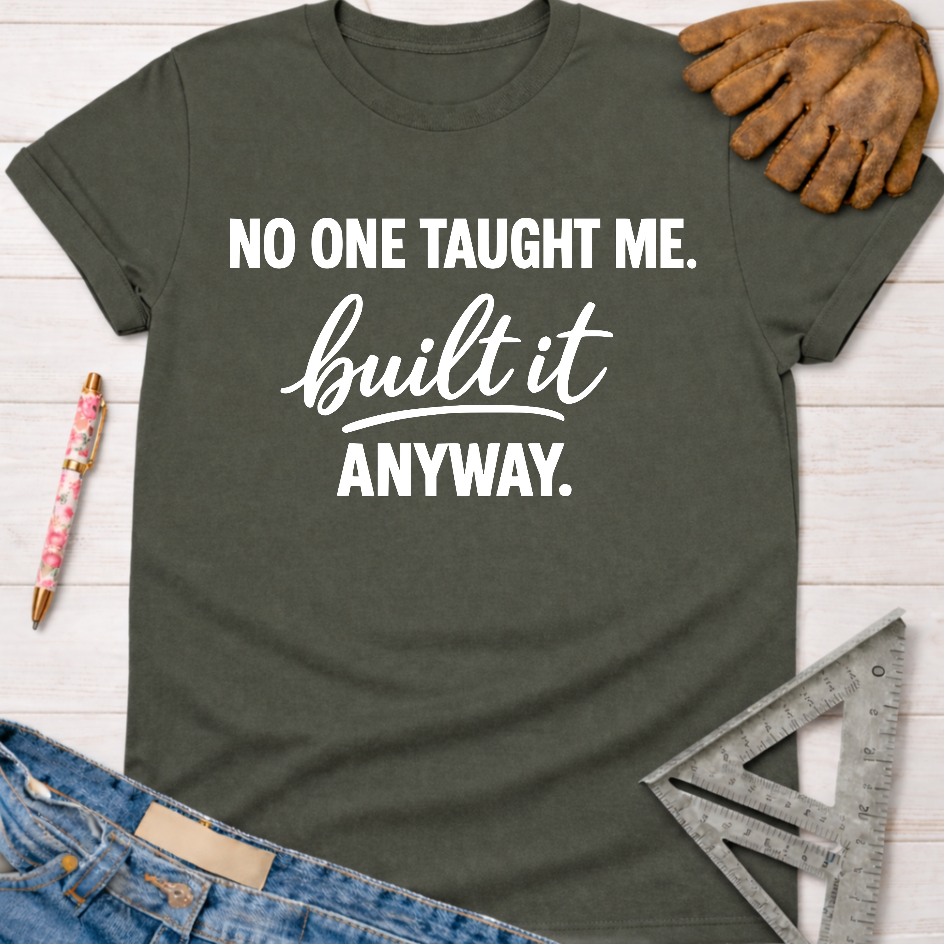 Women's funny woodworking graphic tee shirt for female woodworkers, makers, and DIY builders — Sawdust & Ponytails. Dark gray t-shirt with "NO ONE TAUGHT ME. built it ANYWAY." in white text.