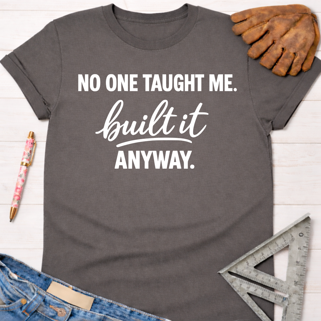 Charcoal gray women's funny woodworking graphic tee shirt with "NO ONE TAUGHT ME. built it ANYWAY." in white text, for female woodworkers, makers, and DIY builders — Sawdust & Ponytails
