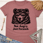 Women's funny woodworking graphic tee shirt for female woodworkers, makers, and DIY builders — Sawdust & Ponytails. Mauve cotton tee with a focused bear in goggles and "Not Angry. Just Focused." text.