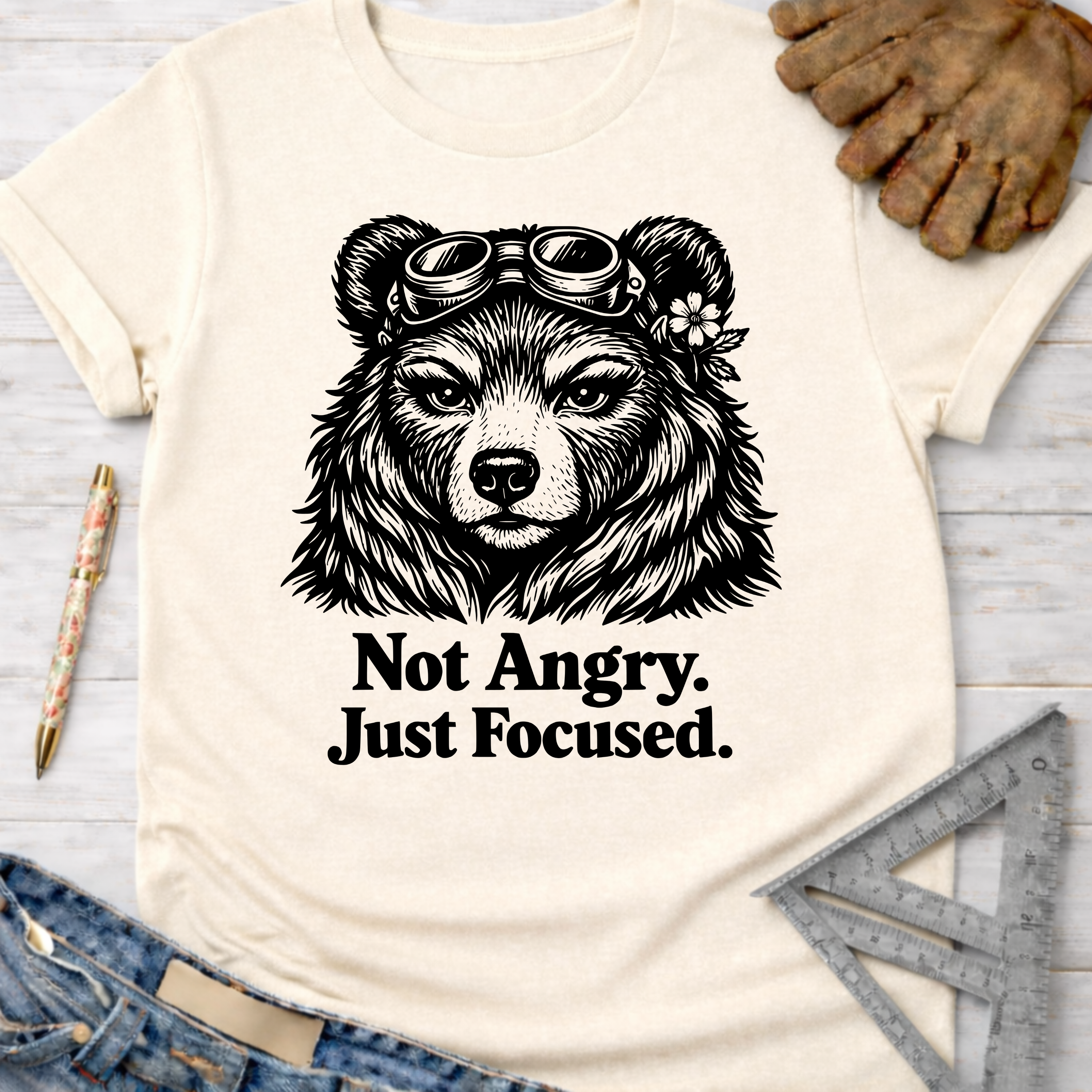 Women's funny woodworking graphic tee shirt for female woodworkers, makers, and DIY builders — Sawdust & Ponytails. Cream t-shirt with a focused bear in goggles and "Not Angry. Just Focused." text.