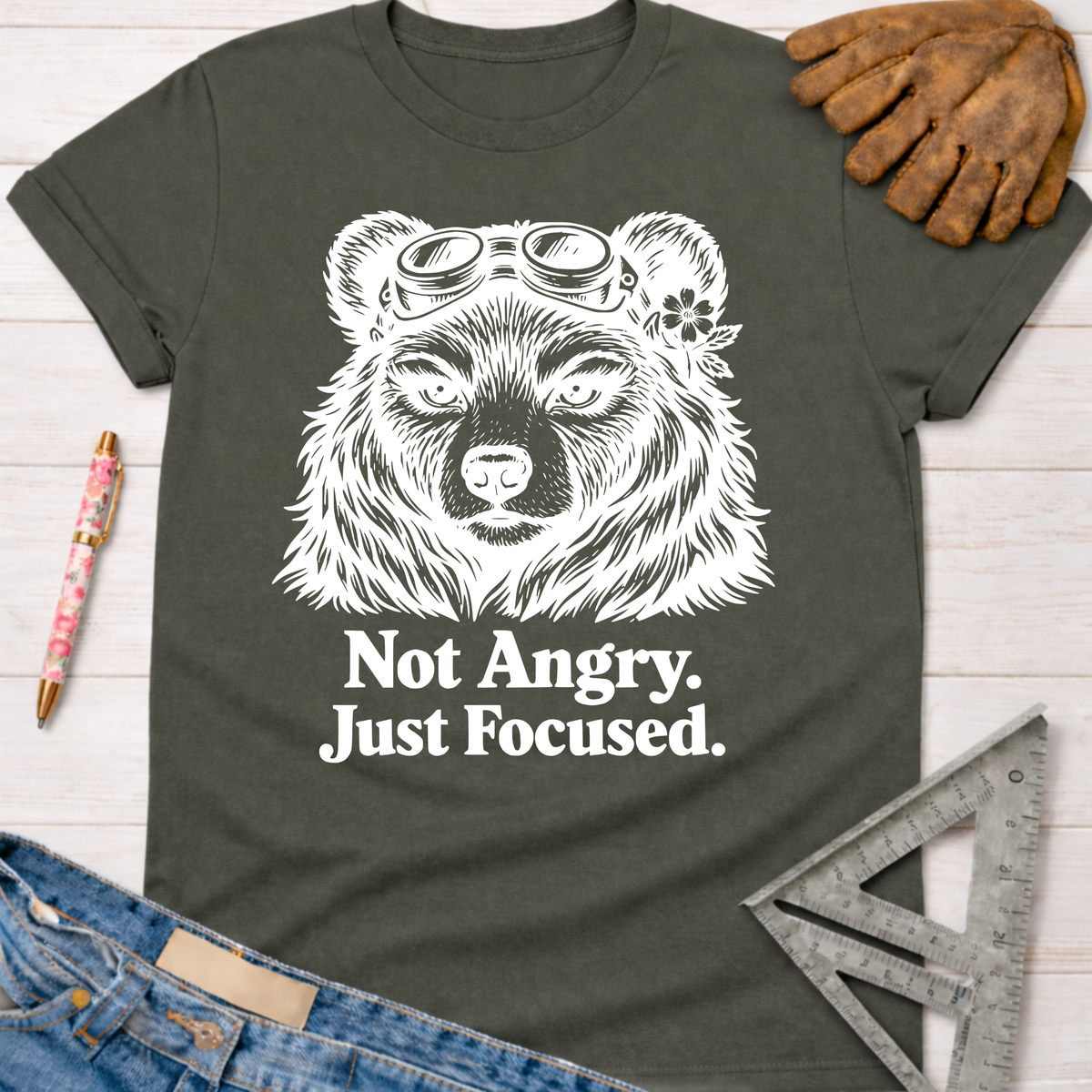 Women's funny woodworking graphic tee shirt for female woodworkers, makers, and DIY builders — Sawdust & Ponytails. Dark gray cotton tee with white "Not Angry. Just Focused." text and a bear wearing goggles and a flower.