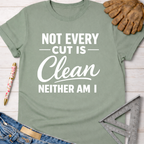 Women's funny woodworking graphic tee shirt for female woodworkers, makers, and DIY builders — Sawdust & Ponytails. Sage green cotton tee with "Not Every Cut Is Clean Neither Am I" in white text.
