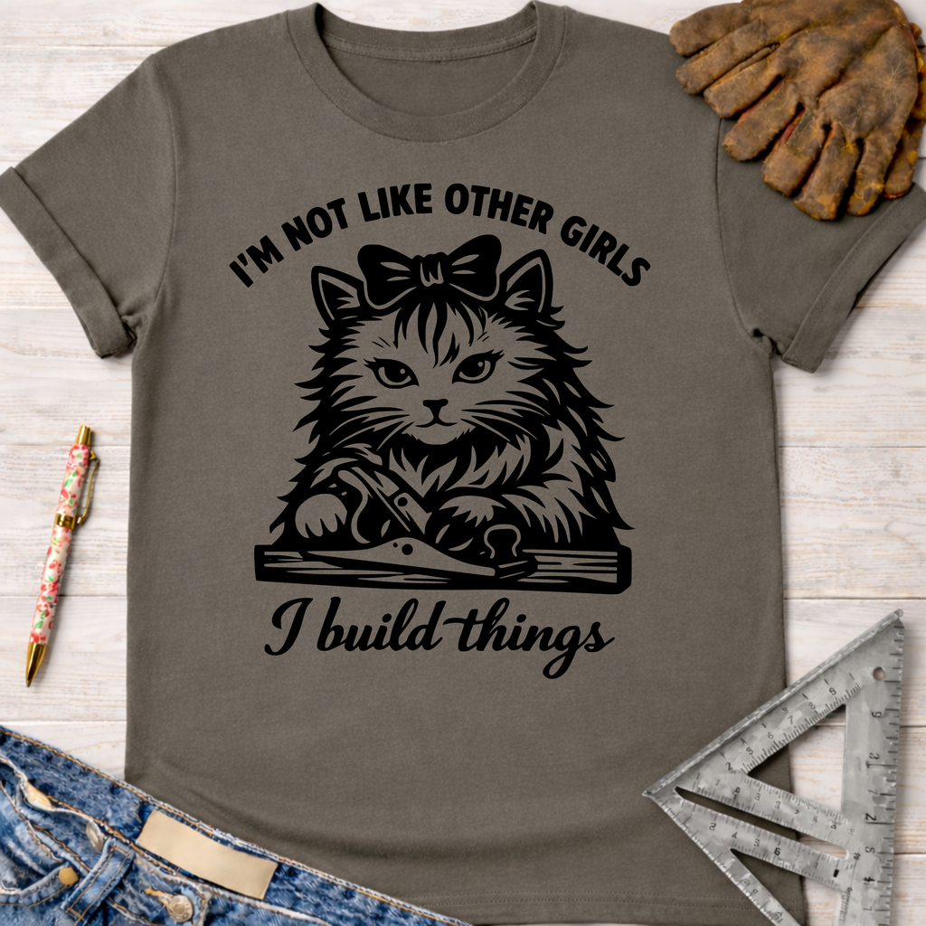 Women's funny woodworking graphic tee shirt for female woodworkers, makers, and DIY builders — Sawdust & Ponytails. Gray cotton tee with "I'm not like other girls, I build things" text and a cat using a hand plane.