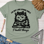 Women's funny woodworking graphic tee shirt for female woodworkers, makers, and DIY builders — Sawdust & Ponytails. Sage green cotton tee with "I'm not like other girls, I build things" text and a cat using a hand plane.