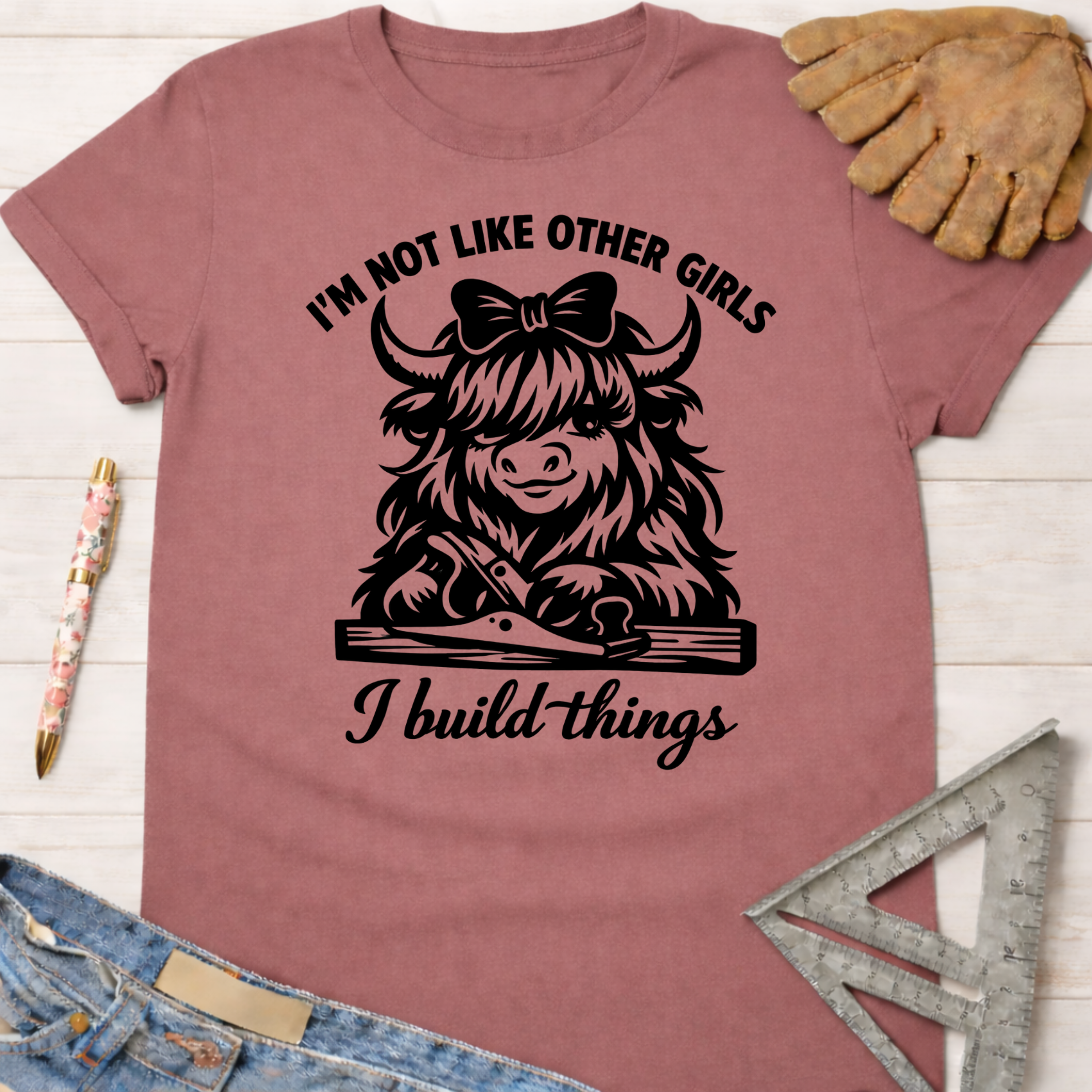 Women's funny woodworking graphic tee shirt for female woodworkers, makers, and DIY builders — Sawdust & Ponytails. Mauve cotton tee with "I'm not like other girls, I build things" text and a cute Highland cow with a bow and hand plane.