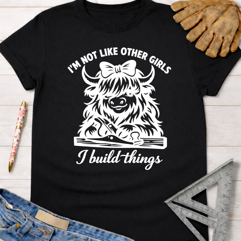 Black cotton tee with "I'm not like other girls, I build things" graphic featuring a Highland cow with a bow and woodworking tools. Women's funny woodworking graphic tee shirt for female woodworkers, makers, and DIY builders — Sawdust & Ponytails