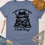 Women's funny woodworking graphic tee shirt for female woodworkers, makers, and DIY builders — Sawdust & Ponytails. Blue cotton tee with "I'm not like other girls, I build things" text and a Highland cow holding a hand plane.