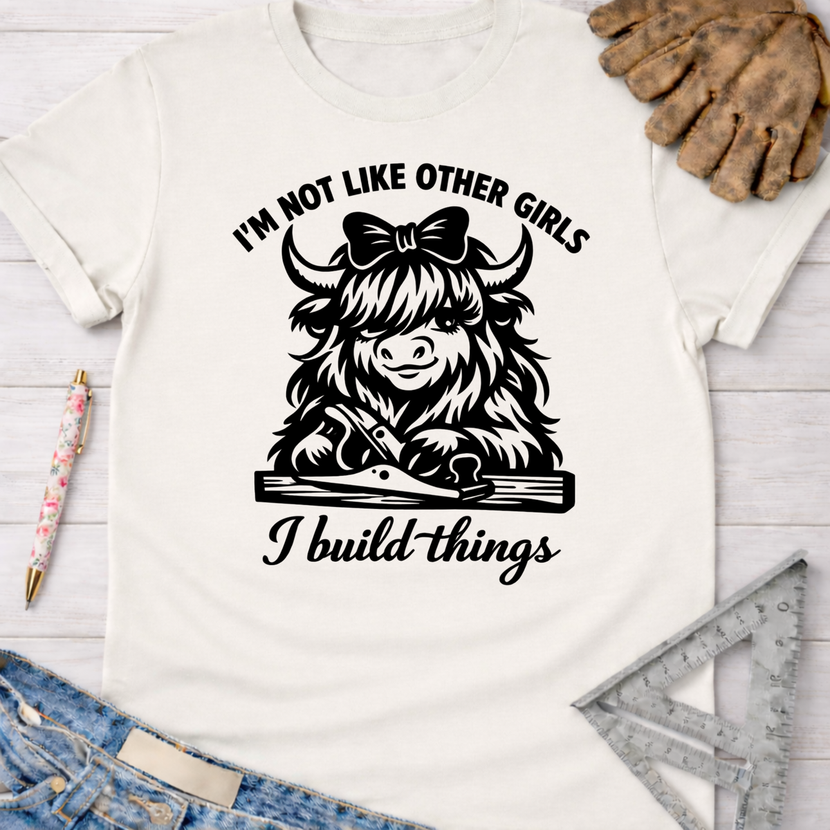 Women's funny woodworking graphic tee shirt for female woodworkers, makers, and DIY builders — Sawdust & Ponytails. White cotton tee with "I'm not like other girls, I build things" and a Highland cow with a bow and hand plane.