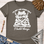 Charcoal gray cotton tee with "I'm not like other girls, I build things" and a Highland cow graphic. Women's funny woodworking graphic tee shirt for female woodworkers, makers, and DIY builders — Sawdust & Ponytails.