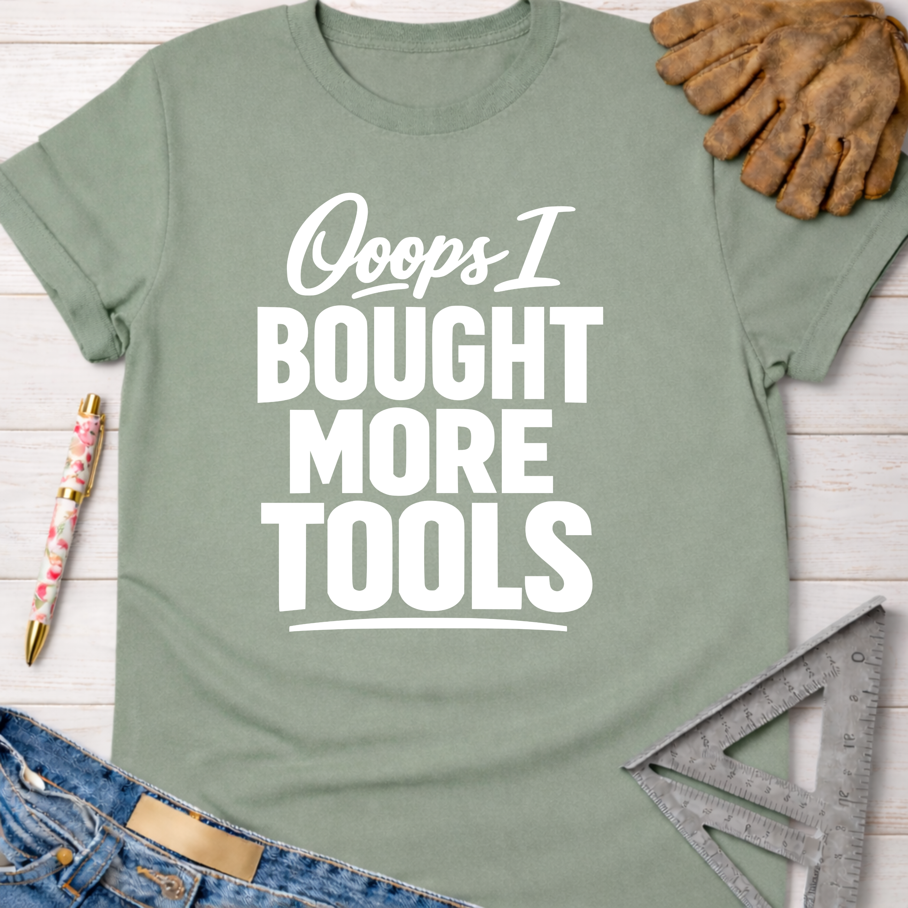 Women's funny woodworking graphic tee shirt for female woodworkers, makers, and DIY builders — Sawdust & Ponytails. Sage green cotton tee with "Ooops I Bought More Tools" in white text.