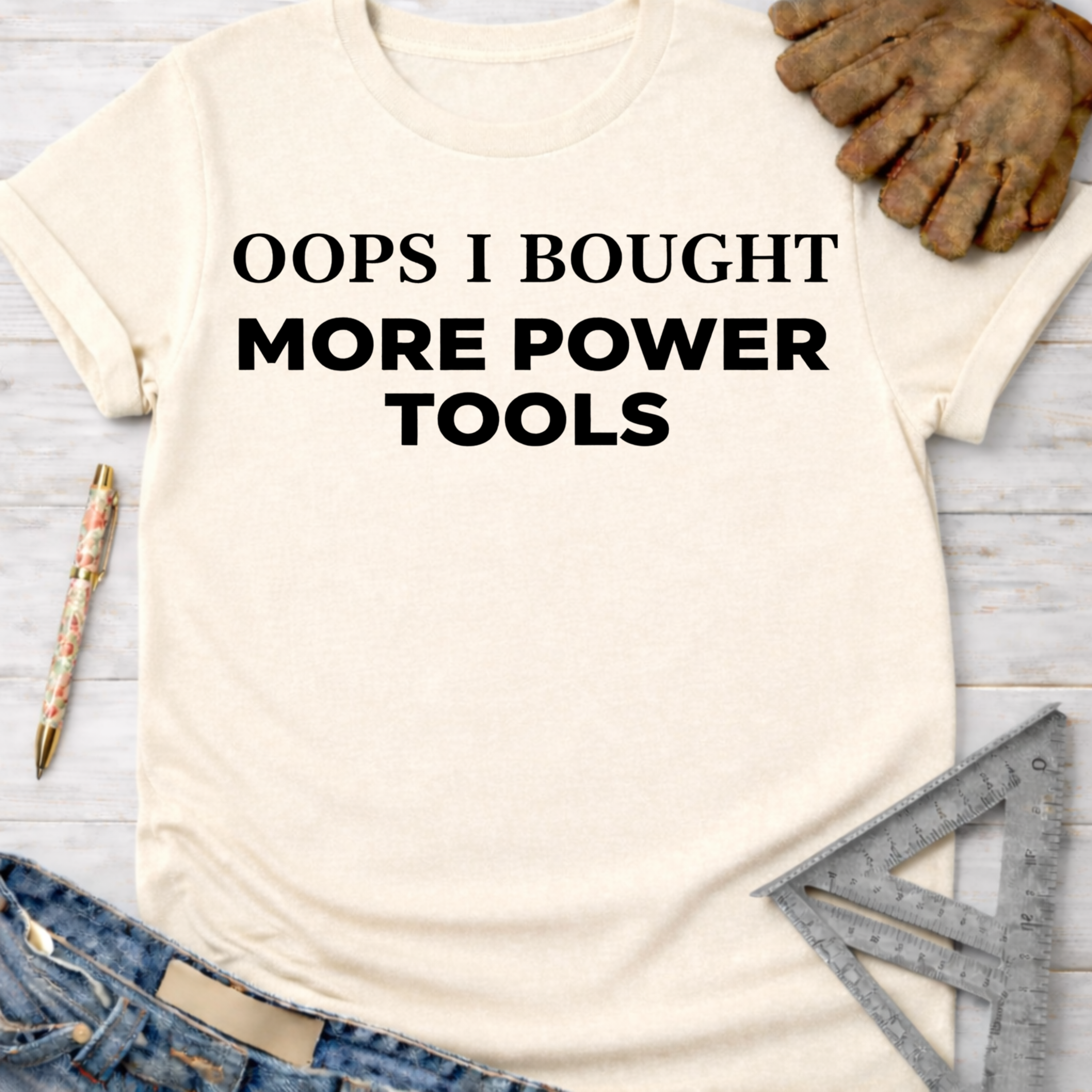 Women's funny woodworking graphic tee shirt for female woodworkers, makers, and DIY builders — Sawdust & Ponytails. Cream t-shirt with "OOPS I BOUGHT MORE POWER TOOLS" in black text.