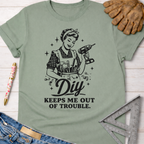 Sage green women's funny woodworking graphic tee with "DIY Keeps Me Out Of Trouble" and a retro woman holding a drill.