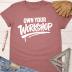Women's funny woodworking graphic tee shirt for female woodworkers, makers, and DIY builders — Sawdust & Ponytails. Mauve cotton t-shirt with "Own Your Workshop" in white text.