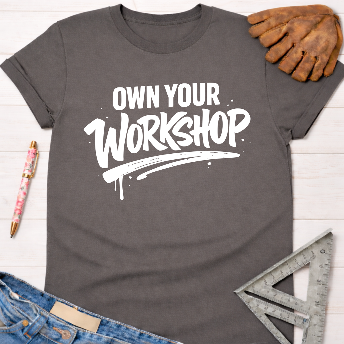 Women's funny woodworking graphic tee shirt for female woodworkers, makers, and DIY builders — Sawdust & Ponytails. Dark gray cotton tee with "Own Your Workshop" in white text.
