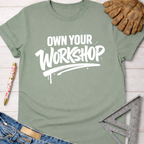 Women's funny woodworking graphic tee shirt for female woodworkers, makers, and DIY builders — Sawdust & Ponytails. Sage green cotton t-shirt with "OWN YOUR WORKSHOP" in white bold text.