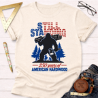Patriotic Sasquatch T-shirt: cream tee with Bigfoot holding a log and axe, "Still Standing 250 years of American Hardwood" text.