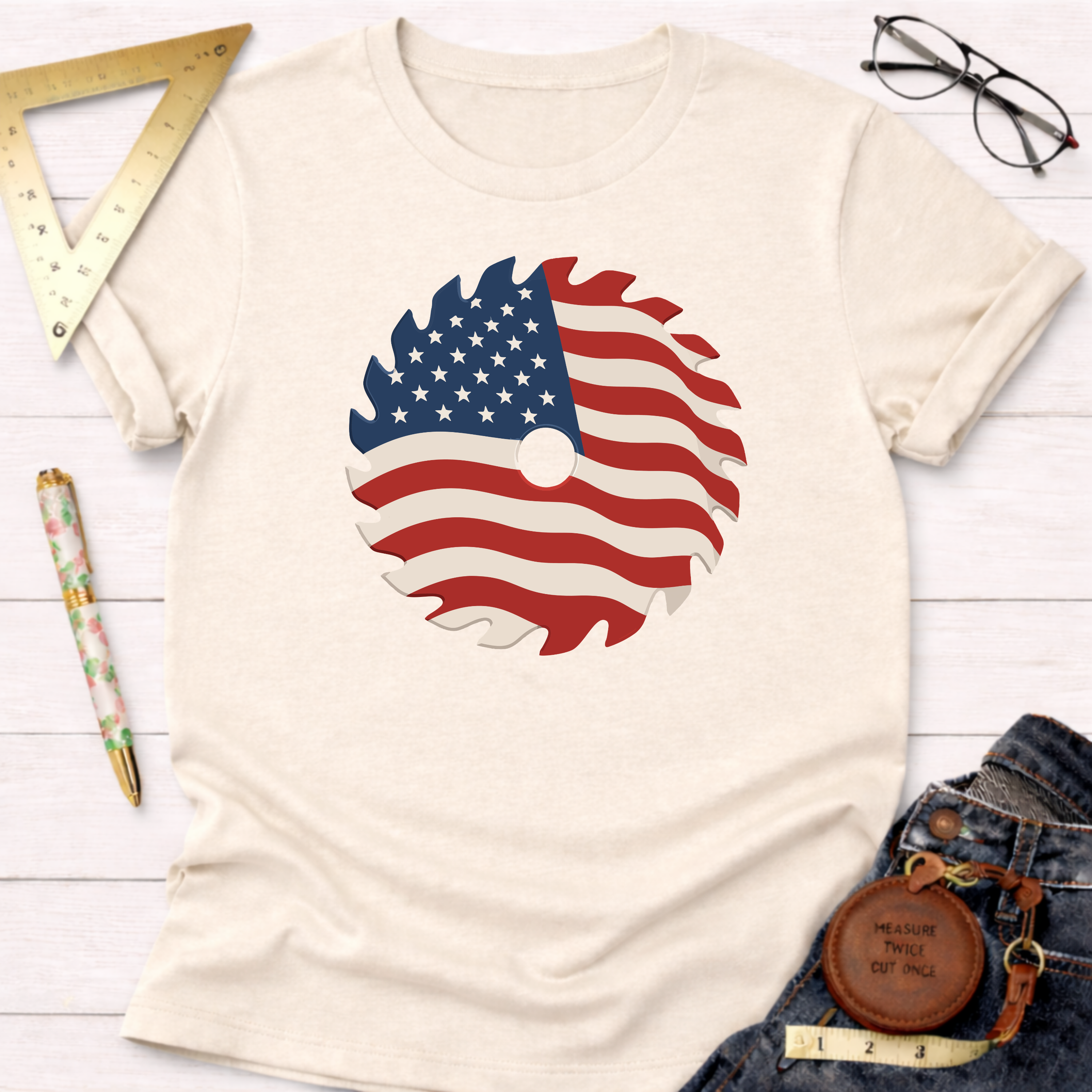 Cream cotton t-shirt with a wavy American flag saw blade graphic, styled with jeans and tools.
