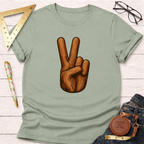 Sage green cotton t-shirt with a wood-textured peace sign graphic, folded on a white wooden surface.