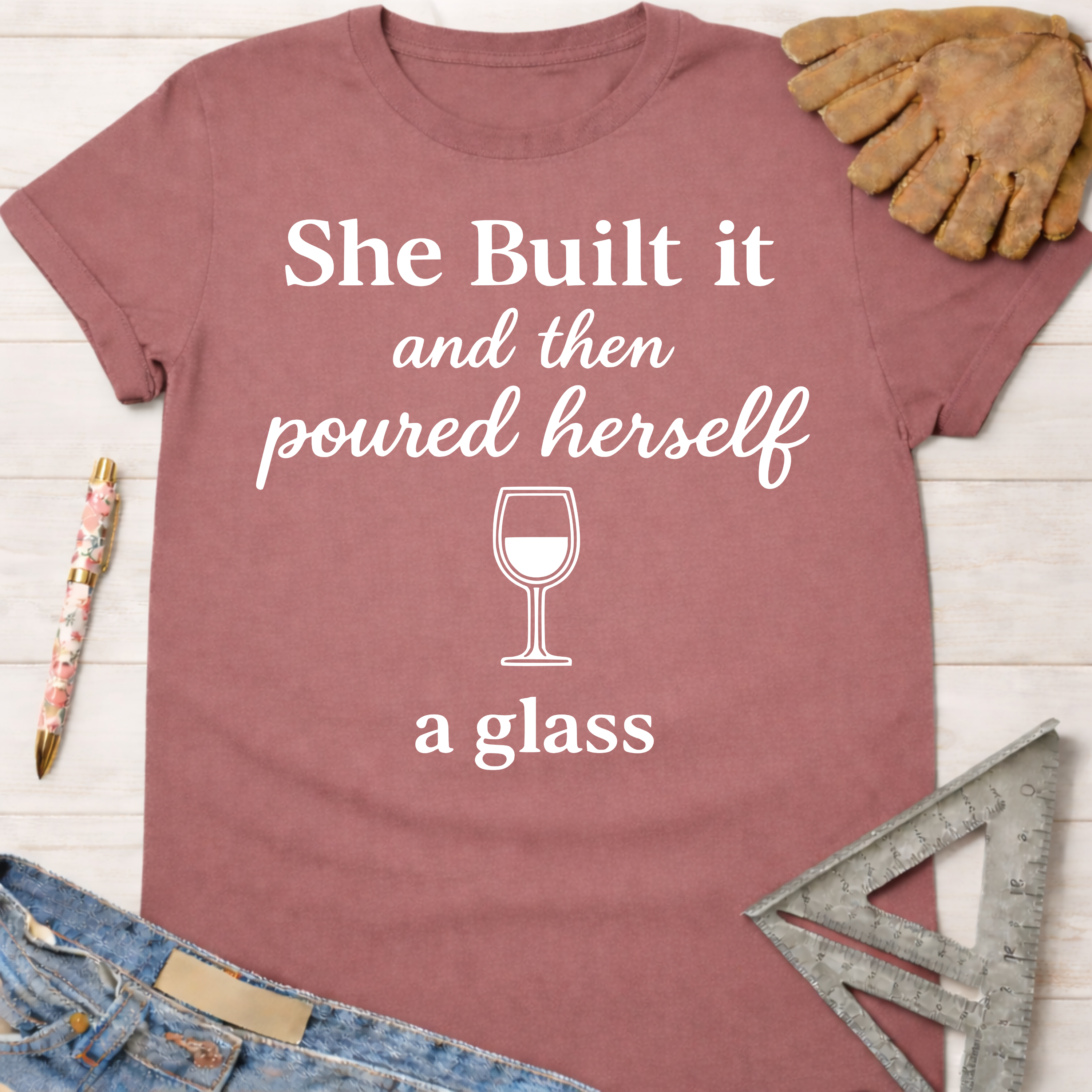 Women's funny woodworking graphic tee shirt for female woodworkers, makers, and DIY builders — Sawdust & Ponytails. Mauve cotton tee with "She Built it and then poured herself a glass" graphic.