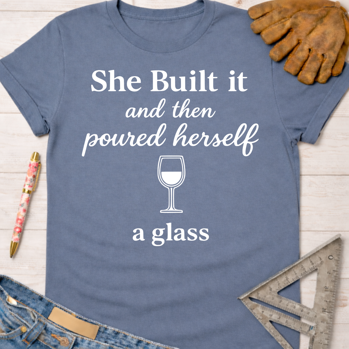 Women's funny woodworking graphic tee shirt for female woodworkers, makers, and DIY builders — Sawdust & Ponytails. Blue cotton tee with "She Built it and then poured herself a glass" graphic.
