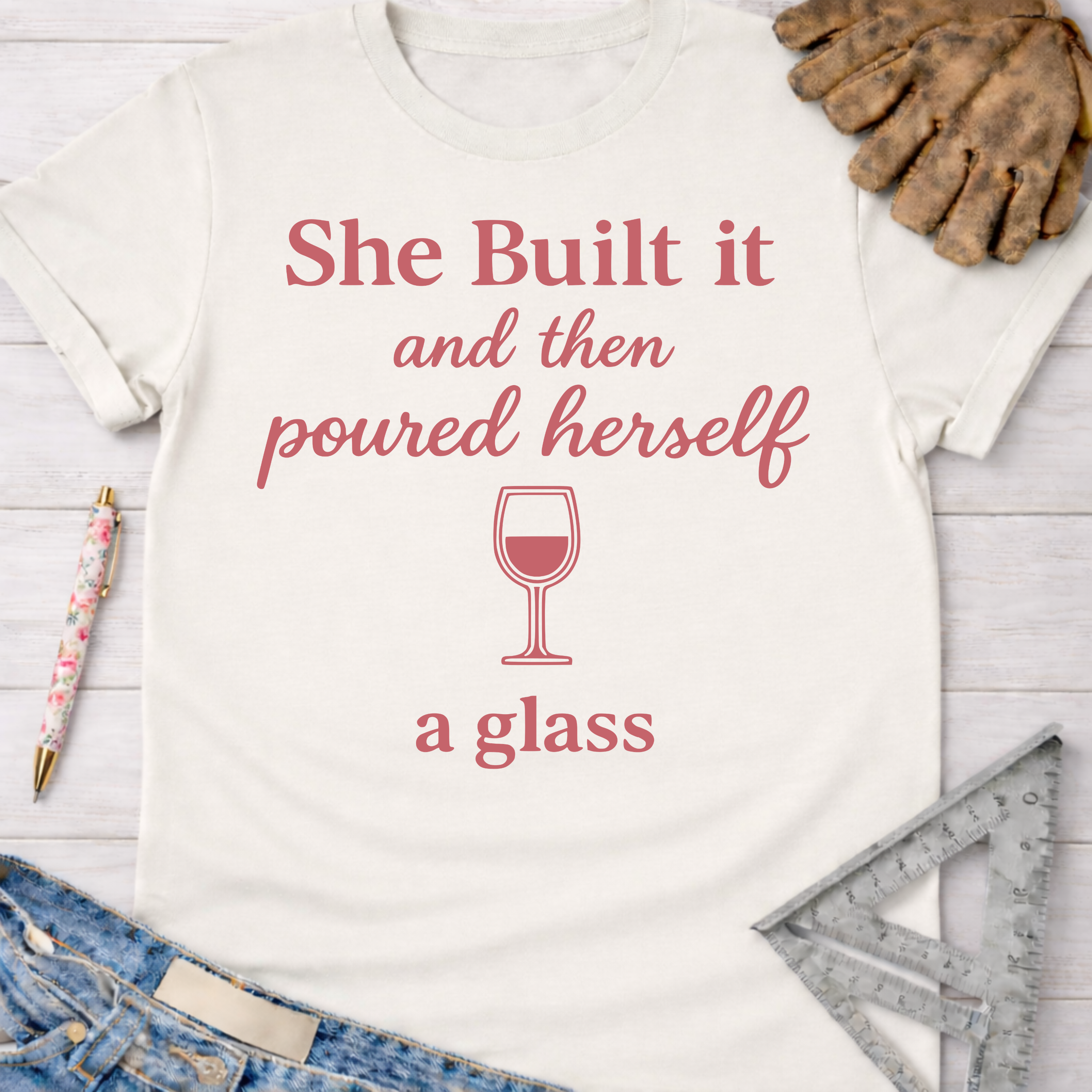Women's funny woodworking graphic tee shirt for female woodworkers, makers, and DIY builders — Sawdust & Ponytails. Cream t-shirt with "She Built it and then poured herself a glass" in pink.