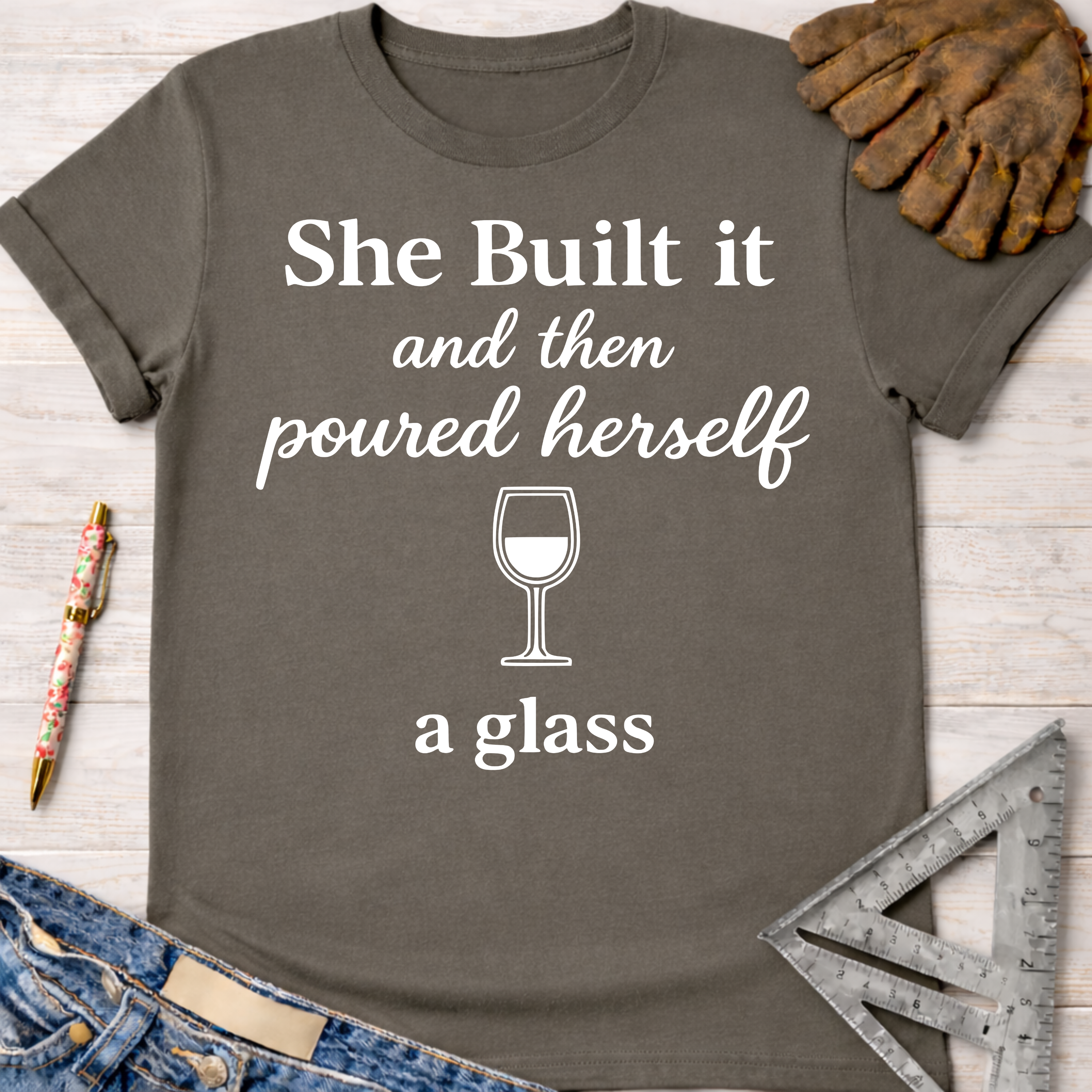 Women's funny woodworking graphic tee shirt for female woodworkers, makers, and DIY builders — Sawdust & Ponytails. Dark gray cotton tee with "She Built it and then poured herself a glass" text and wine glass graphic.