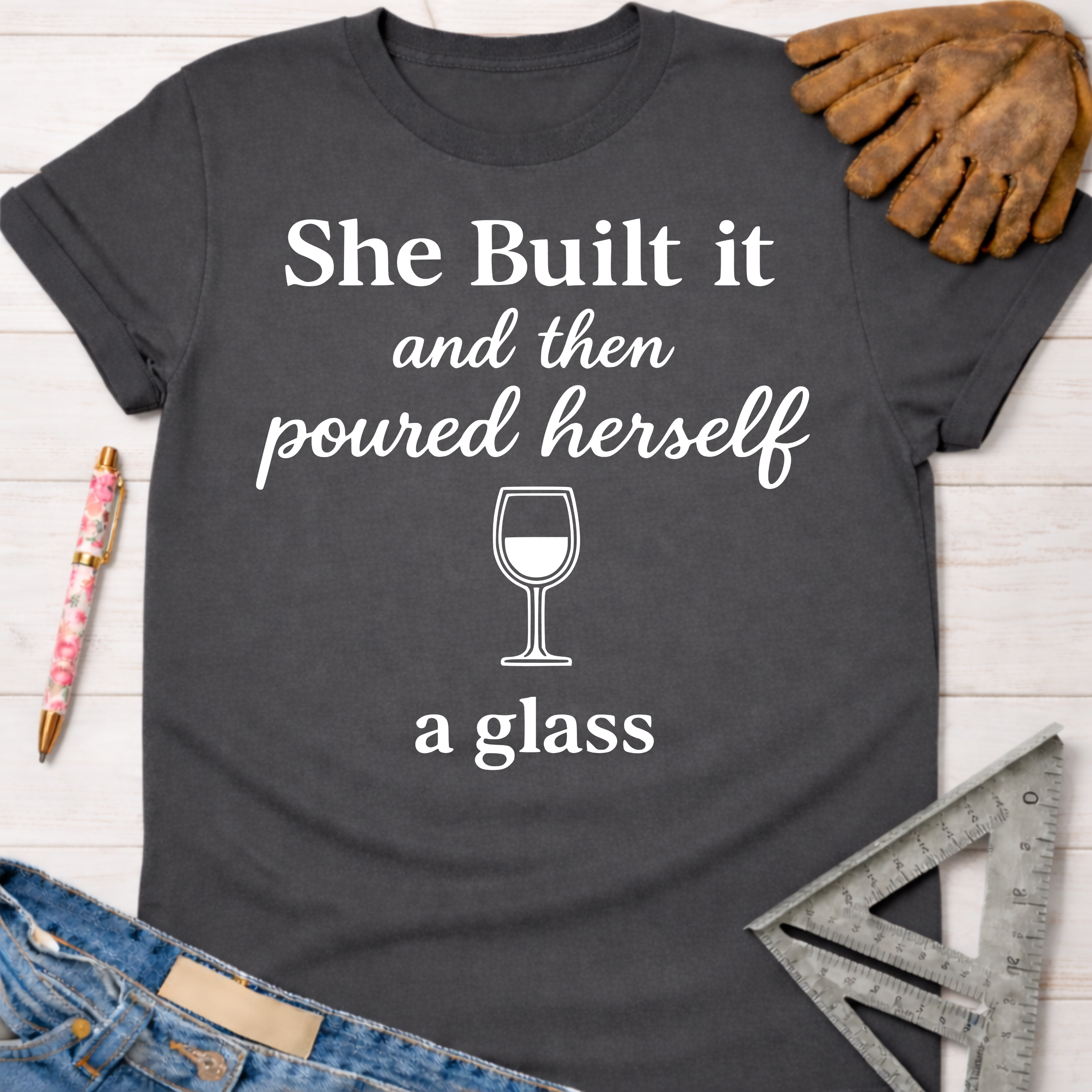 Women's funny woodworking graphic tee shirt for female woodworkers, makers, and DIY builders — Sawdust & Ponytails. Dark gray cotton tee with "She Built it and then poured herself a glass" text and wine glass graphic.
