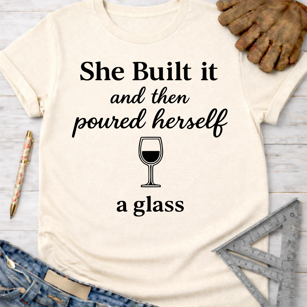 Women's funny woodworking graphic tee shirt for female woodworkers, makers, and DIY builders — Sawdust & Ponytails. Cream t-shirt with "She Built it and then poured herself a glass" text and wine glass graphic.