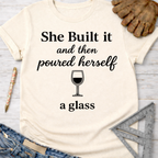 Women's funny woodworking graphic tee shirt for female woodworkers, makers, and DIY builders — Sawdust & Ponytails. Cream t-shirt with "She Built it and then poured herself a glass" text and wine glass graphic.