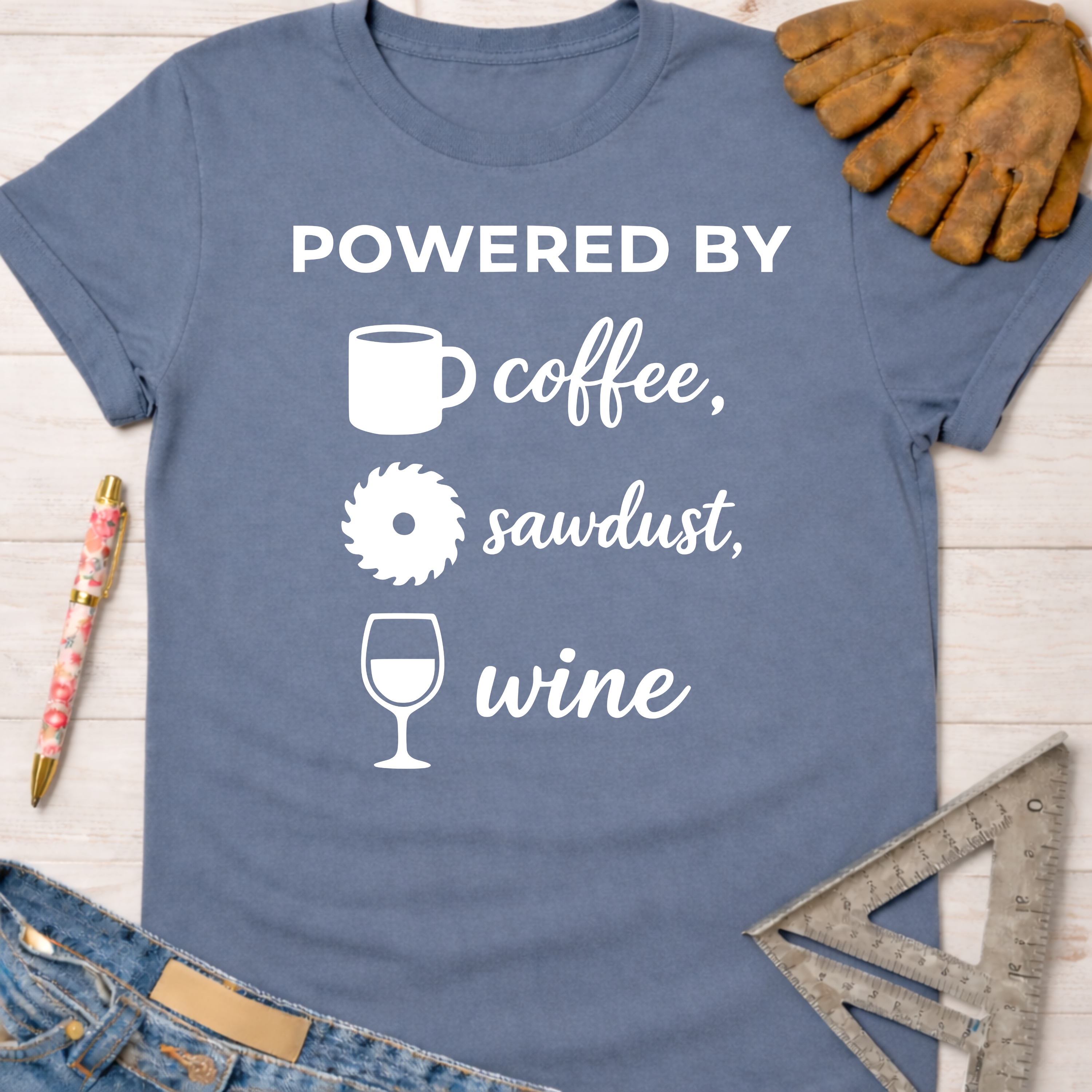 Women's funny woodworking graphic tee shirt for female woodworkers, makers, and DIY builders — Sawdust & Ponytails. Blue cotton tee with "Powered By coffee, sawdust, wine" graphic.