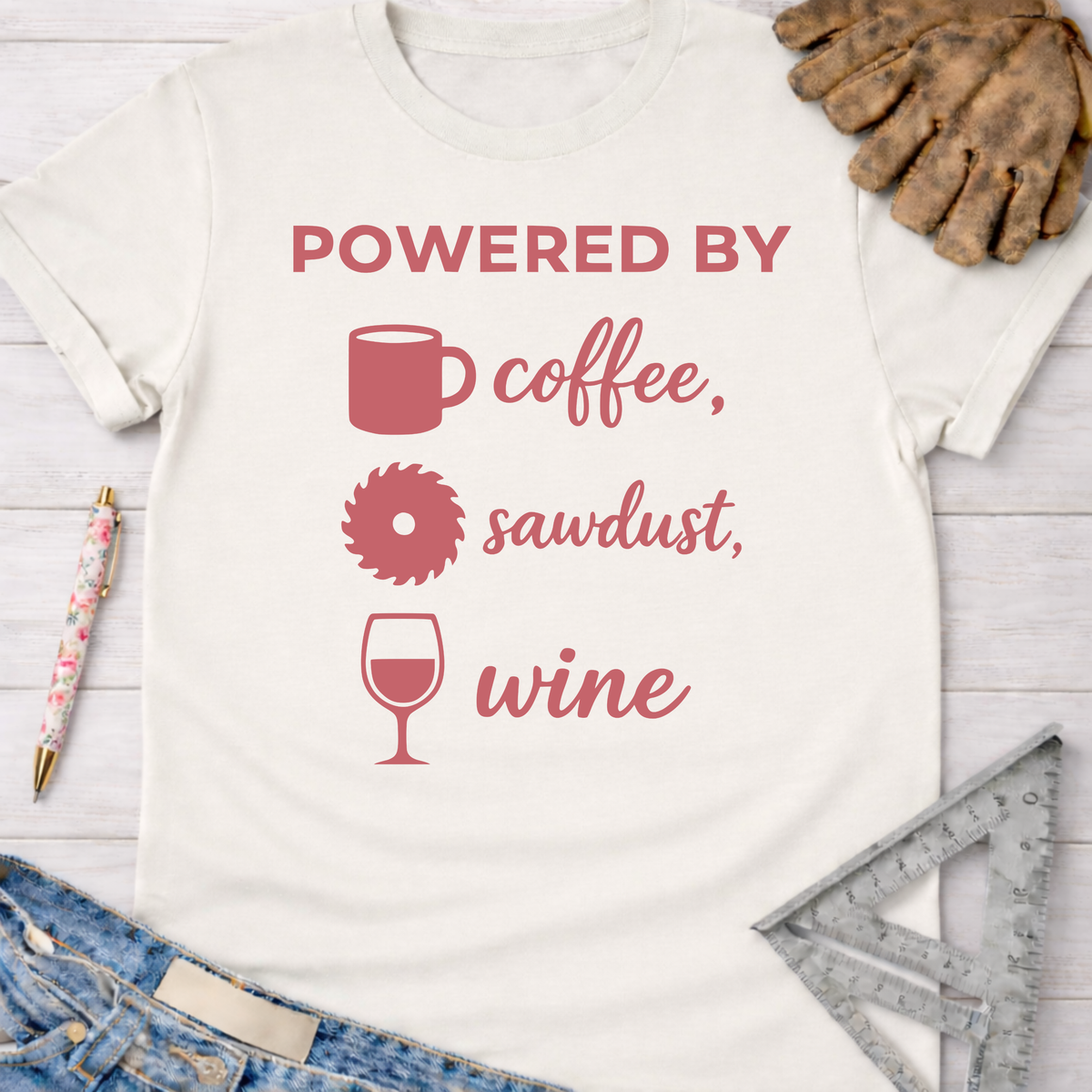 Women's funny woodworking graphic tee shirt for female woodworkers, makers, and DIY builders — Sawdust & Ponytails. White cotton tee with "Powered By coffee, sawdust, wine" in pink.