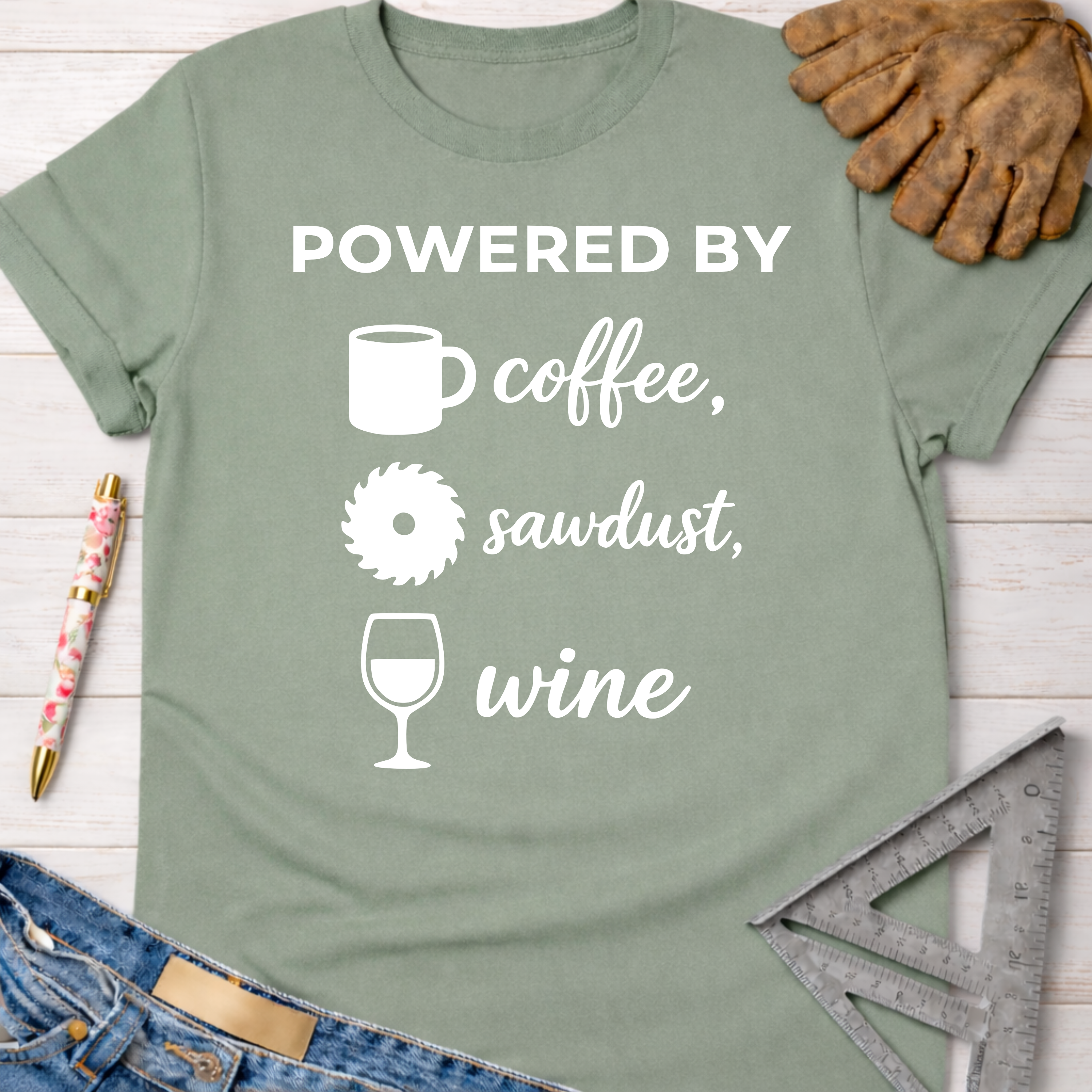 Women's funny woodworking graphic tee shirt for female woodworkers, makers, and DIY builders — Sawdust & Ponytails. Sage green cotton tee with "Powered By coffee, sawdust, wine" graphic.