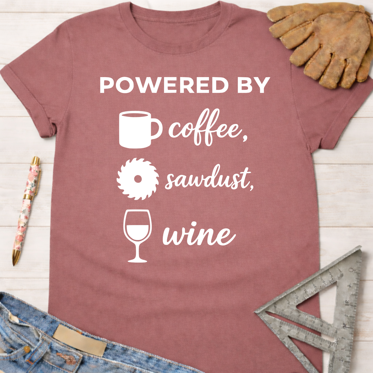 Women's funny woodworking graphic tee shirt for female woodworkers, makers, and DIY builders — Sawdust & Ponytails. Mauve t-shirt with "Powered By coffee, sawdust, wine" graphic.