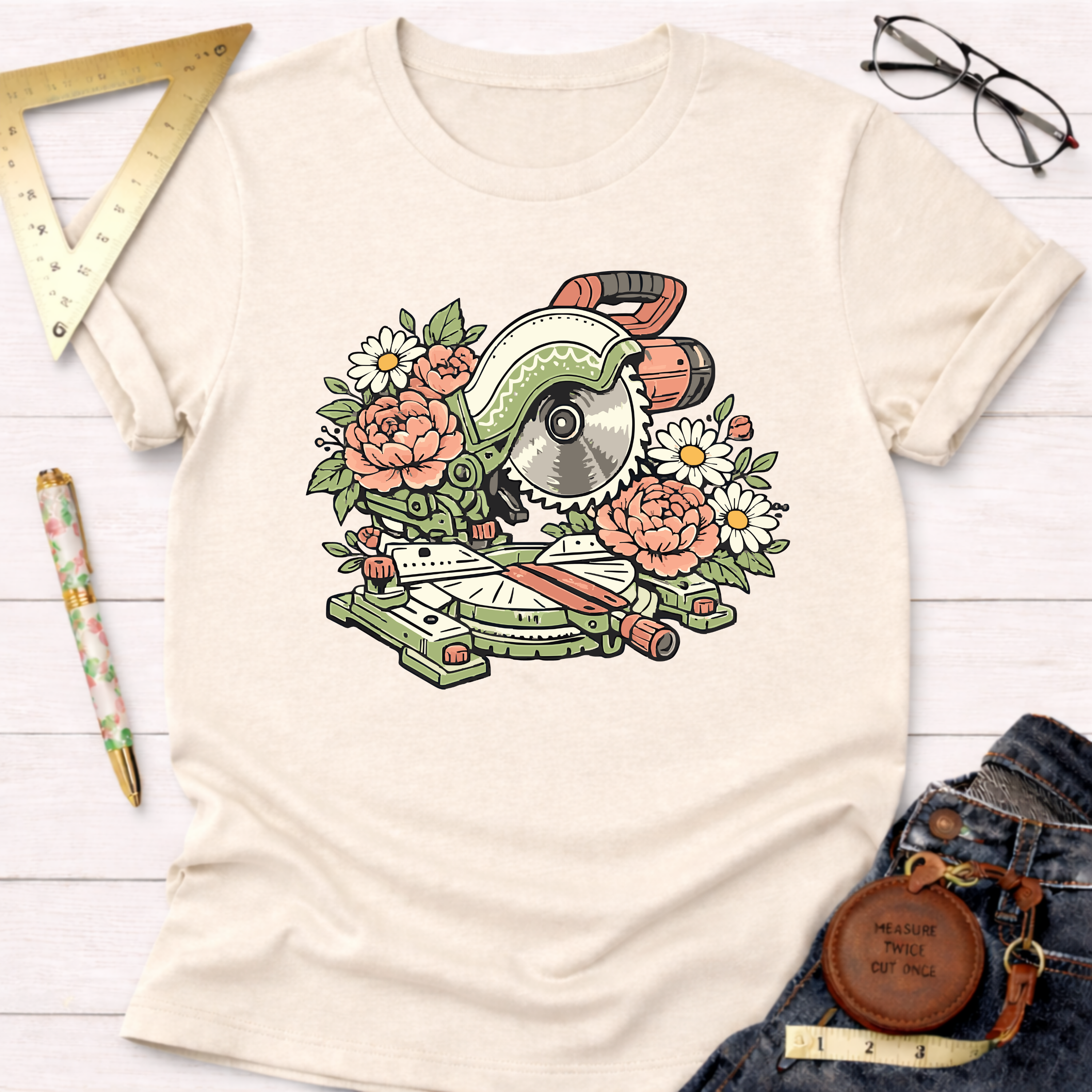 Cream t-shirt with a green miter saw design surrounded by pink and white flowers.
