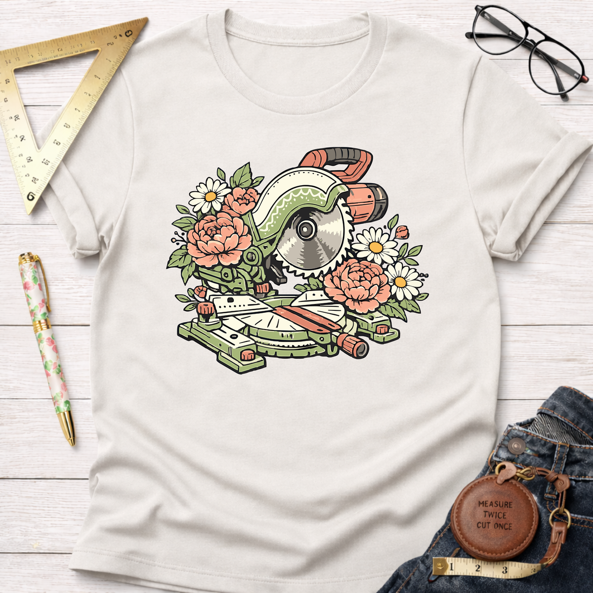 White cotton t-shirt with a colorful floral miter saw graphic, surrounded by woodworking tools.
