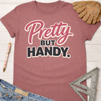 Women's funny woodworking graphic tee shirt for female woodworkers, makers, and DIY builders — Sawdust & Ponytails. Mauve pink cotton tee with "Pretty But Handy" in pink and black script.