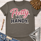 Women's funny woodworking graphic tee shirt for female woodworkers, makers, and DIY builders — Sawdust & Ponytails. Dark gray cotton t-shirt with "Pretty BUT HANDY" in pink and black.
